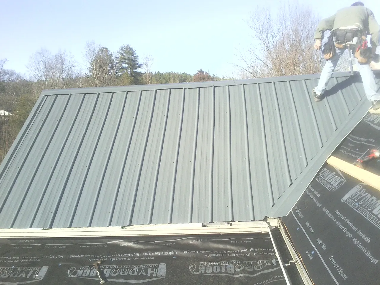 Crew installing dark green standing seam panels over synthetic underlayment in Stanford