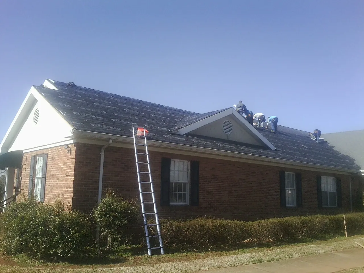 Crew tearing shingles off a brick ranch roof with a ladder set — Emergency Roof Repair work by our crew in Stanford