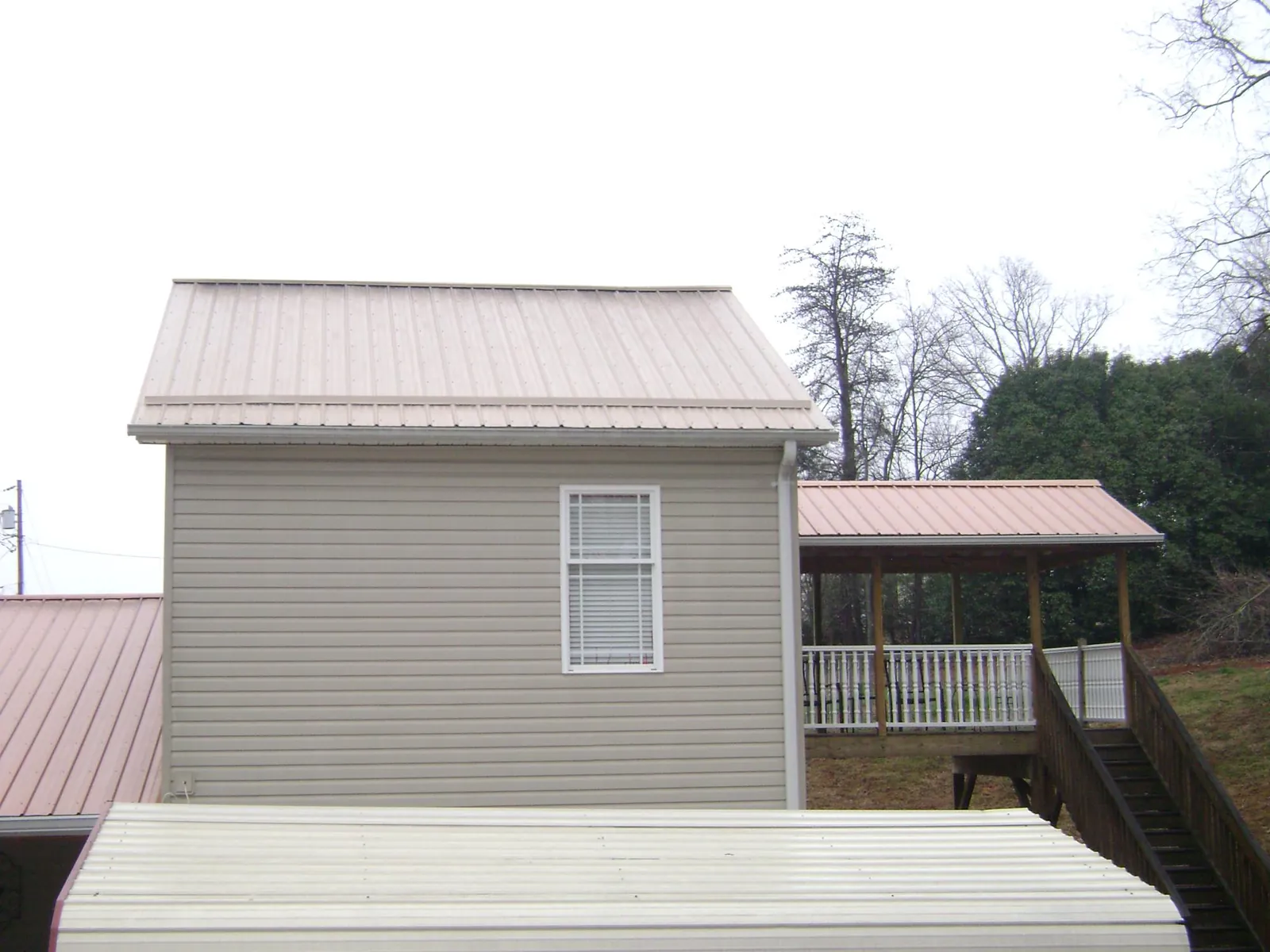 Tan metal roofs on a two story addition and attached porch, from a Roof Replacement job in Stanford